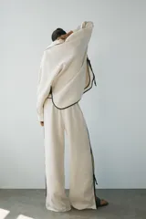 Camisa de lino color crudo con cuello solapa, manga larga y bajo asimétrico. Presenta detalles de ribetes negros a contraste y aberturas laterales con tiras para ajustar.