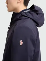 Campera impermeable Moncler Grenoble modelo Shipton, de color azul marino, con capucha alta, cierre frontal termo sellado, bolsillos laterales con cremallera y puños elásticos.