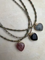 Collar de tres niveles compuesto por cuentas pequeñas de piedra natural y metal, con tres dijes en forma de corazón de piedra natural facetada en tonos rosado, negro y gris, enmarcados en metal dorado.