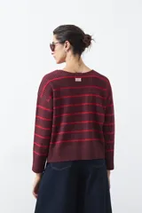 Sweater de tejido de punto con diseño de rayas horizontales en tonos bordó y rojo. Presenta cuello redondo, mangas largas con hombros caídos y terminaciones acanaladas en puños, cuello y ruedo.
