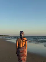 Vestido largo de silueta ajustada, con estampado abstracto en tonos azules, morados y naranjas. Presenta un escote drapeado profundo y tirantes finos.