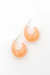 Par de caravanas con diseño de argolla gruesa y abierta, confeccionadas en resina color salmón con acabado brillante y cierre de presión con perno.