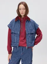 Campera de denim a rayas verticales con cuello de pana en color bordó. Presenta cierre frontal, mangas desmontables con cierre en los hombros, canesú en el pecho y bolsillos de parche cuadrados.