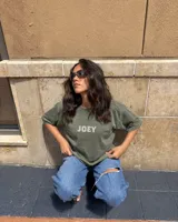Remera oversize gris oscuro con corte holgado, mangas cortas y estampa trasera en blanco y negro con forma de estampilla que muestra a una persona con un gato y el texto 'Kaboa Industries'.
