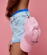 Gorra tipo bucket de sarga color rosa pálido, con visera curva y la palabra "Lover" bordada en negro en la parte frontal.