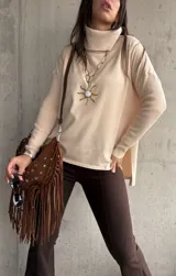 Polera de tejido de punto color beige, con cuello alto, mangas largas y aberturas laterales en el ruedo.