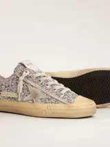 Zapatillas bajas Golden Goose modelo V-Star, cubiertas de glitter plateado, con estrella lateral en cuero color crema y suela de goma color caramelo.