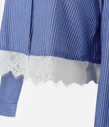 Camisa cropped azul con rayas diplomáticas blancas, cuello clásico, mangas largas y detalle de encaje blanco aplicado en el borde inferior.