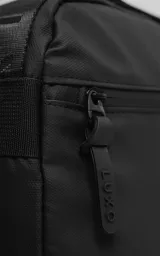 Bolso cruzado (bandolera) negro de tela sintética, con correa ajustable estampada con la palabra "LUXO". Presenta un diseño estructurado con bolsillo frontal y parche con logo en la base.