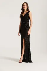 Vestido largo negro de fiesta con lentejuelas, escote en V cruzado, sin mangas y tajo pronunciado en la pierna izquierda.