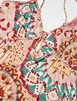 Vestido largo con estampado caleidoscópico en tonos rosa, rojo y verde. Presenta tirantes finos, escote en V, corte imperio y falda con volantes. Incluye detalle de trenzas en el pecho y la cintura que se anudan en la espalda descubierta.