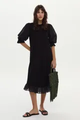 Vestido midi de corte recto color negro, con mangas cortas abullonadas, cuello redondo y detalle de volado en el ruedo.