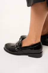 Mocasines negros de charol arrugado con horma redondeada y detalle de presilla con hebilla y ojalillos.