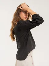 Blusa blanca de algodón con escote redondo, manga tres cuartos y silueta oversized. Presenta bordados y texturas combinadas.