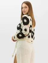 Buzo de tejido crochet con diseño de motivos circulares en contraste blanco y negro, con apliques de pedrería en el centro de los círculos. Presenta corte recto, cuello redondo y manga larga.