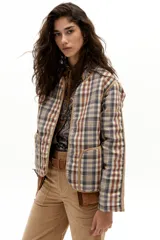 Chaqueta reversible con un lado de twill de lana a cuadros en tonos beige, marrón y gris, con vivos en pana color camel y bolsillos frontales. El otro lado es de algodón capitoneado con estampado de arabescos. Tiene cuello a la base y botones metálicos a presión escondidos.