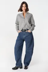 Jean de corte wide leg y tiro alto, confeccionado en denim azul con sutil textura rayada vertical. Presenta diseño de cinco bolsillos, cierre frontal con botón y costuras reforzadas.