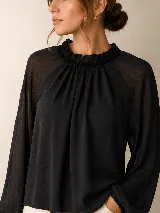 Blusa negra de manga larga confeccionada en tela liviana y semitransparente, con cuello alto fruncido y volados. Presenta un diseño fluido con mangas amplias y puños elásticos.