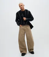 Pantalón masculino de corte barrel, confeccionado en sarga de algodón color beige. Presenta un diseño de piernas anchas con volumen en la cadera y leve entalle hacia el bajo, cintura con pasantes, cierre frontal con botón y bolsillos funcionales.