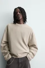 Sudadera de corte boxy fit confeccionada en tejido de mezcla de algodón, con cuello redondo y mangas largas. Presenta un diseño minimalista con texto estampado a contraste en el pecho y efecto lavado.