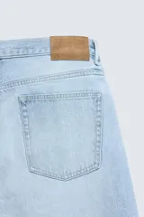 Jeans de denim de algodón, tiro medio, color celeste claro lavado. Corte recto y holgado desde la cadera hasta el tobillo, con rotura en una de las perneras. Presenta cierre frontal con cremallera y botón, y cinco bolsillos.