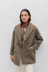 Tapado de paño de lana color marrón con silueta oversize y hombros caídos. Presenta doble abotonadura frontal, solapas amplias con detalle en contraste azul, y mangas con ajuste en los puños.