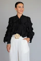 Camisa negra de tela liviana con diseño de volados verticales en el frente y mangas, cuello con lazo ajustable y puños con botones.