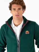 Campera de polar verde oscuro con cierre frontal, cuello alto con ribete rojo y logo bordado en el pecho.
