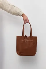 Bolso tipo tote de cuero vacuno con textura granulada, color tostado. Presenta doble asa larga para llevar al hombro y un diseño amplio y minimalista.