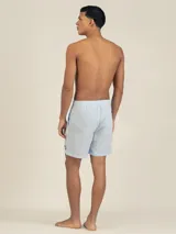 Short de baño celeste con rayas verticales blancas y parche bordado en la pierna derecha.