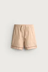 Shorts relaxed fit color beige con textura en relieve tipo jacquard, cintura elástica con cordón ajustable y detalle de bordado en contraste en el bajo.