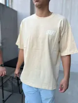 Remera negra de corte oversize con estampa gráfica en la espalda. El diseño presenta una silueta lineal de un ángel, el logo Dropz Corp. en tipografía script, un bloque de microtexto y un código de barras gráfico.