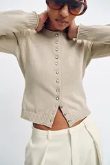Chaqueta de punto de cuello redondo y manga larga, con cierre frontal de botones metálicos y acabados en rib.