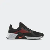 Championes de entrenamiento Reebok Flip Charge, color negro con detalles en naranja coral. Presentan una malla transpirable en la parte superior, refuerzos laterales y una entresuela robusta en gris claro con el logo de Reebok en naranja en la parte trasera.