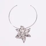 Gargantilla tipo collar rígido plateado, con un dije central grande con forma de flor con pétalos irregulares y textura.