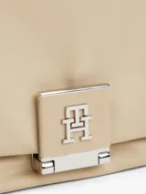 Cartera de hombro color beige claro, con acabado liso y solapa frontal con cierre de pinza metálico que presenta el monograma TH. Incluye una correa tejida ajustable y extraíble, y una correa de cadena metálica.