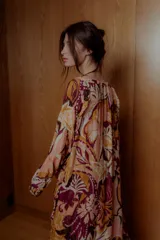 Maxi vestido estilo boho con estampado floral en tonos rosa, naranja y borgoña. Tiene mangas largas sueltas, escote redondo con volados y falda larga con volados.