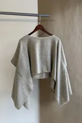 Poncho color beige con diseño a cuadros, cuello bote y terminaciones desflecadas. Tiene aberturas para los brazos en los laterales y detalles en cuero.