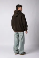 Buzo canguro de corte oversize, confeccionado en frisa de algodón con efecto de lavado gastado. Presenta un aplique decorativo cosido al corte en el centro del pecho, capucha amplia y bolsillo frontal tipo canguro.