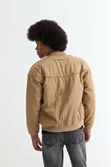 Campera tipo bomber color beige, confeccionada en nylon, con cierre frontal, cuello, puños y ruedo acanalados.