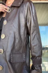 Tapado de cuero ovino color chocolate con detalles de pasamanería y presillas en gamuza al tono. Presenta cierre frontal con botones grandes y mangas largas con puños ajustados.