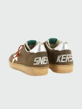 Zapatillas deportivas Golden Goose modelo Ball Star, estilo retro de baloncesto. Cuerpo de gamuza marrón, con estrella lateral blanca y talón plateado. Cordones naranjas y suela de goma desgastada.