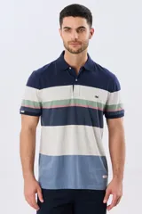 Remera polo de manga corta con diseño de franjas horizontales en tonos azul, beige, verde y terracota. Presenta cuello camisero con cierre frontal de dos botones y un pequeño bordado en el pecho.