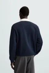 Sudadera de manga larga estilo polo con diseño de rayas horizontales anchas en azul marino y blanco. Presenta cuello de solapa en contraste, cierre frontal con botones ocultos y acabados en rib en puños y bajo.