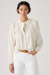 Blusa color crudo de manga larga, con cuello mao y detalles de encaje y bordados en el frente. Presenta diseño abotonado oculto y mangas abullonadas con puños elásticos.