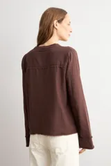 Blusa de manga larga color marrón con cuello redondo y cierre frontal con alamares. Presenta costuras visibles y diseño estructurado.