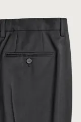Pantalón de traje regular fit negro, confeccionado en lana italiana, con bolsillos laterales, bolsillos traseros de vivo con botón y cierre frontal de cremallera y botón.