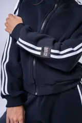 Campera tipo bomber color marrón, con cierre frontal completo, cuello alto y bandas laterales blancas en las mangas. Presenta puños y ruedo acanalados.