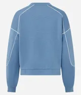 Buzo deportivo de corte oversized en color azul, con cuello redondo, manga larga y puños ajustados. Presenta detalles de frisos contrastantes en color blanco que recorren las mangas y el cuerpo de la prenda.