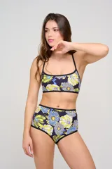 Top de bikini con estampa floral en tonos amarillos, azules y blancos sobre base negra, con diseño enterito al frente y tiras cruzadas en la espalda.